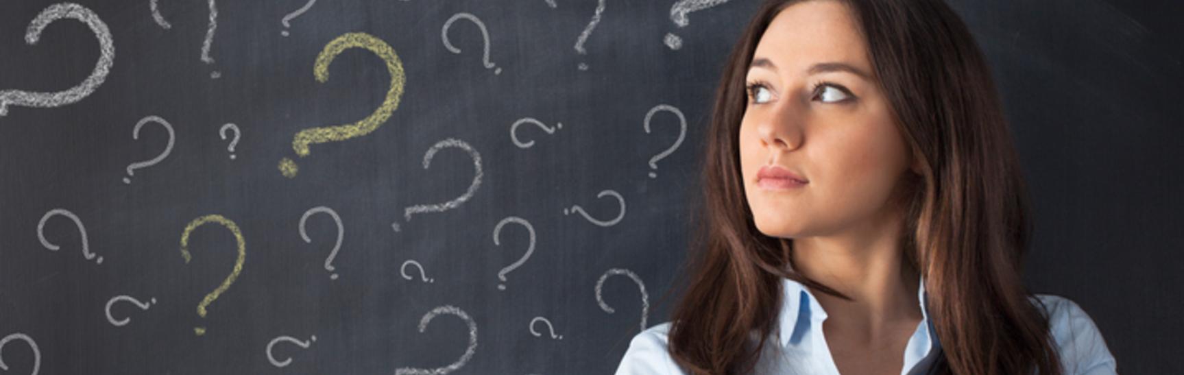 Thinking business woman in front of question marks drawn on blackboard